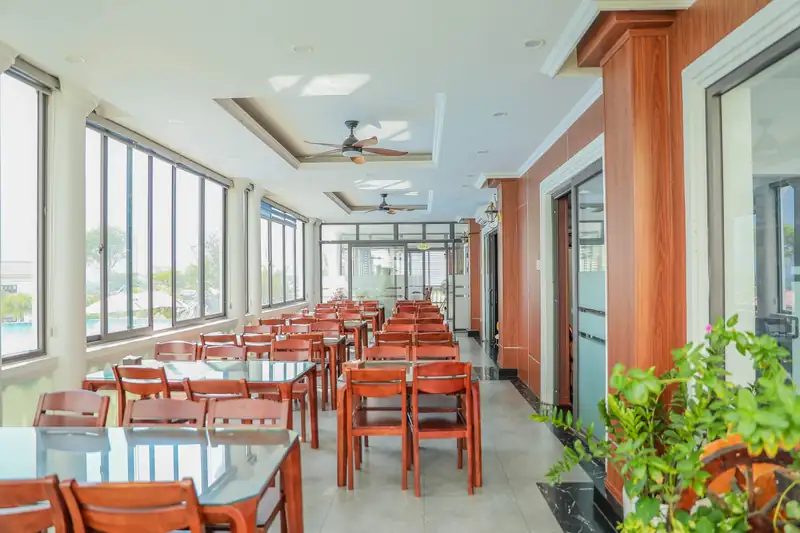 Gian ăn sáng sủa trong nhà hàng Glory: bàn ghế gỗ đỏ xếp dãy, cửa sổ lớn và chậu cây xanh