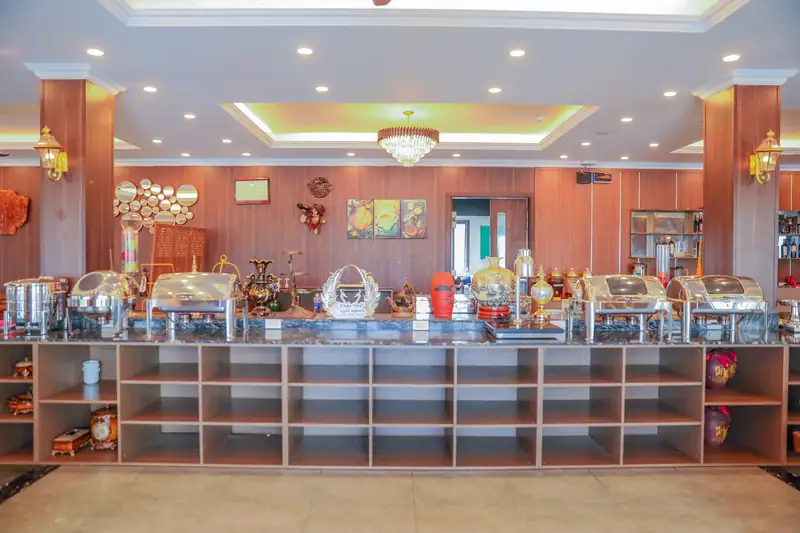 Quầy bày món trong nhà hàng Glory với các nồi giữ nóng inox, kệ gỗ chứa bát đĩa phía dưới