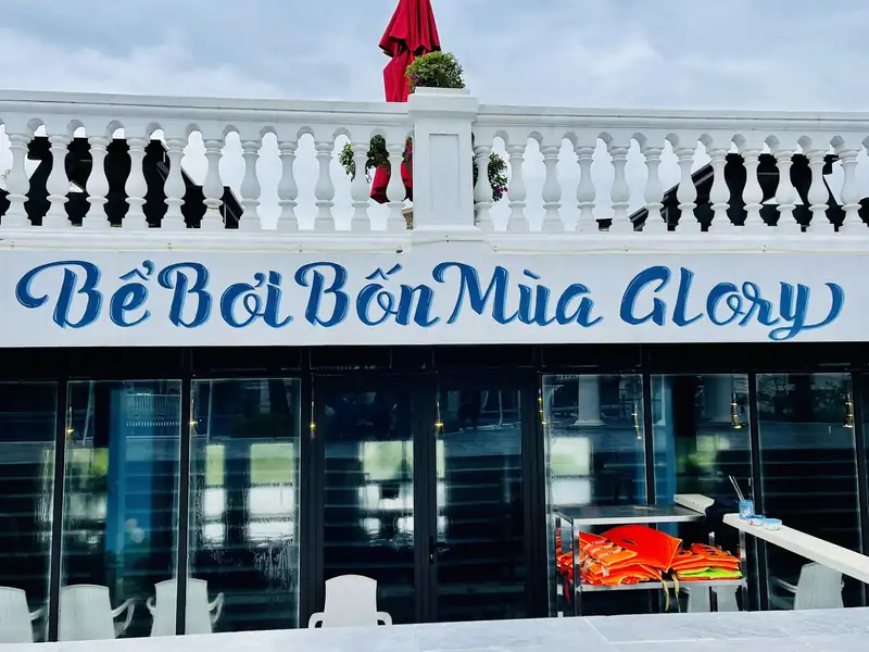 Biển tên Bể Bơi Bốn Mùa Glory gắn dưới lan can trắng, phía dưới là cửa kính của khu bể trong nhà