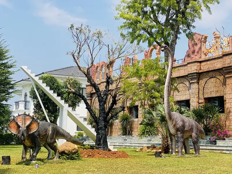 Mô hình khủng long trên bãi cỏ trước bức tường gạch vòm khu Đấu trường La Mã ở Glory Resort