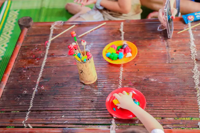 Bàn tre với ống cắm tò he vừa nặn, đĩa bột màu và tay bé đang chọn màu