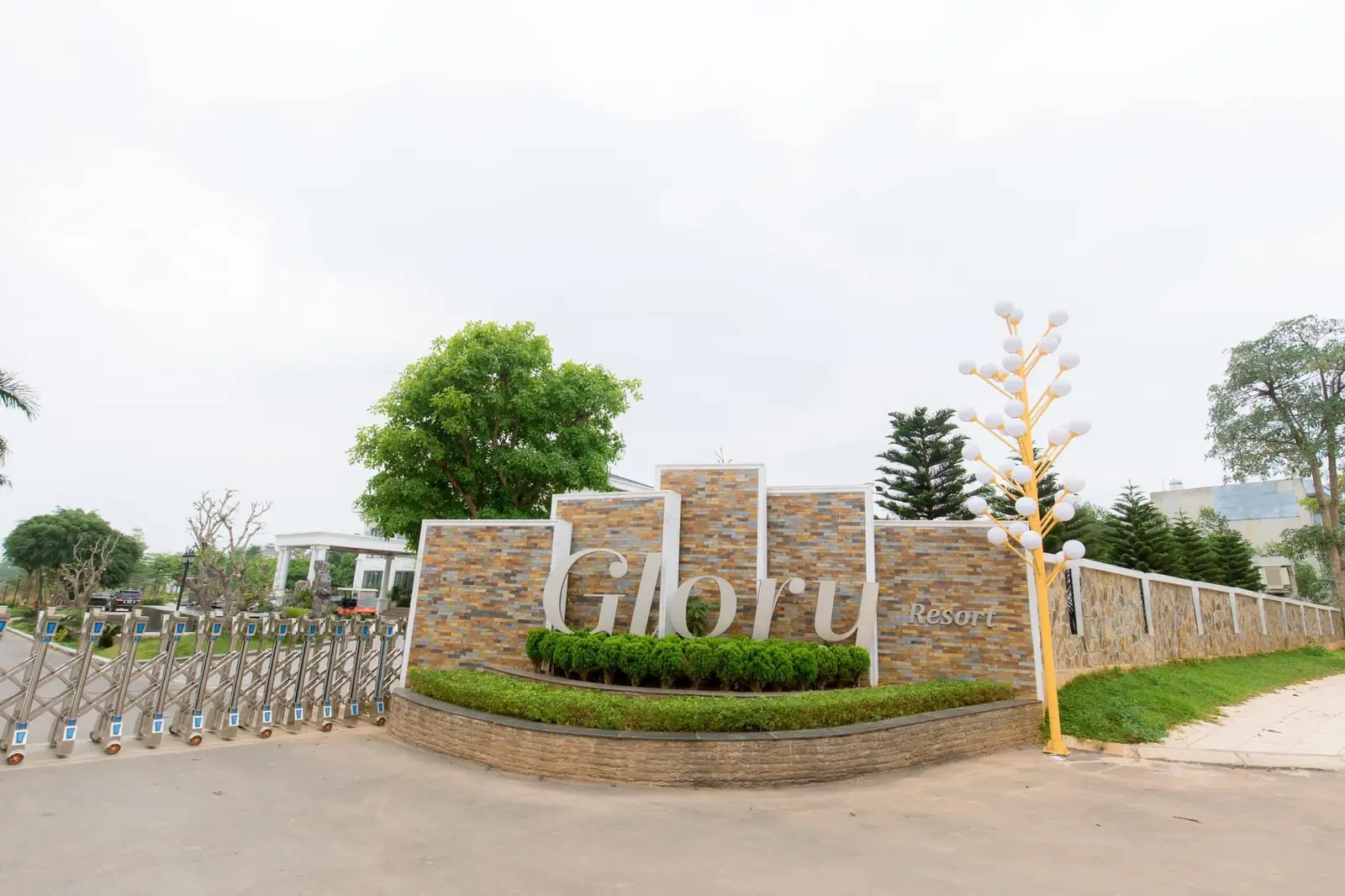 Cổng vào Glory Resort ốp đá, chữ Glory lớn, hàng cây và đèn trang trí hai bên lối vào