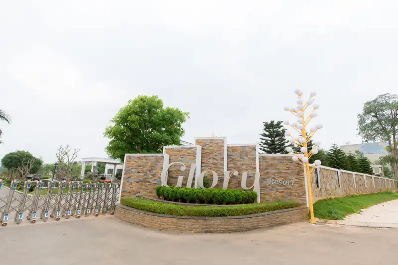 Cổng vào Glory Resort ốp đá, chữ Glory lớn, hàng cây và đèn trang trí hai bên lối vào