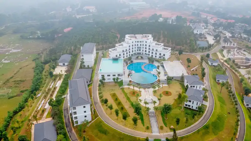 Glory Resort nhìn từ flycam: tòa nhà trắng tân cổ điển, bể bơi lòng cong, vườn và các dãy nhà quanh đồi