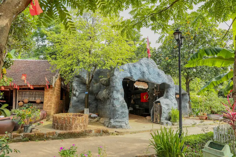 Lối vào hầm rượu Glory Resort dạng hang đá nhân tạo giữa vườn cây, cạnh nhà mái ngói