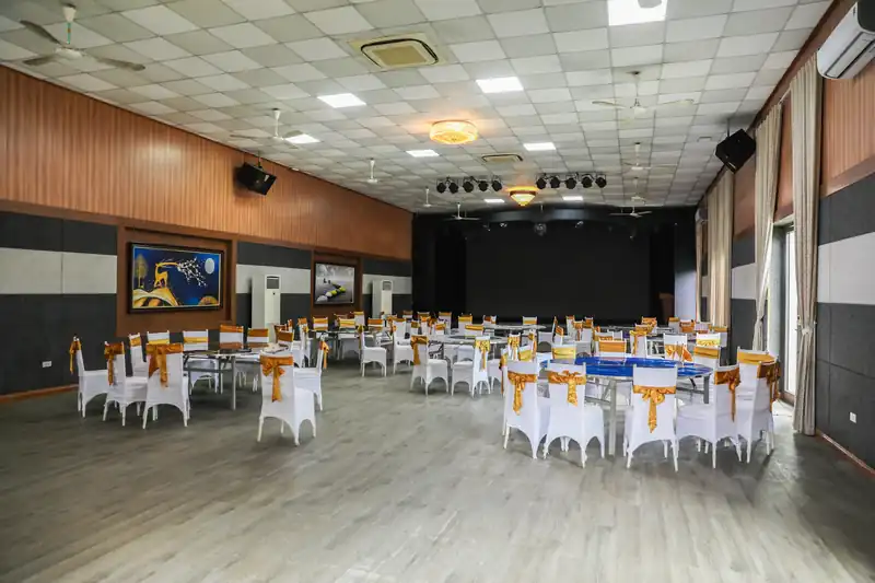 Hội trường Glory Resort kê bàn tròn ghế bọc nơ vàng, sân khấu và hệ đèn phía cuối