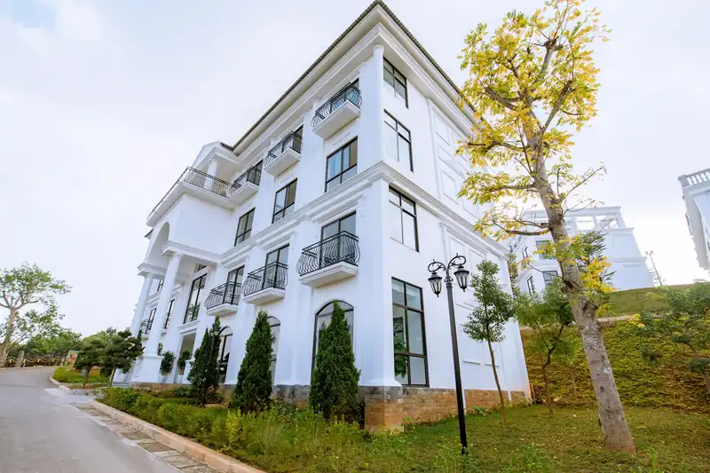 Tòa nhà Home Garden bốn tầng sơn trắng, ban công sắt uốn, cây hoa vàng ven đường nội khu