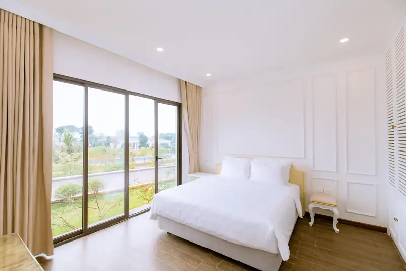 Phòng ngủ LakeSide Villa tường trắng, vách kính lớn nhìn ra hồ và cây xanh