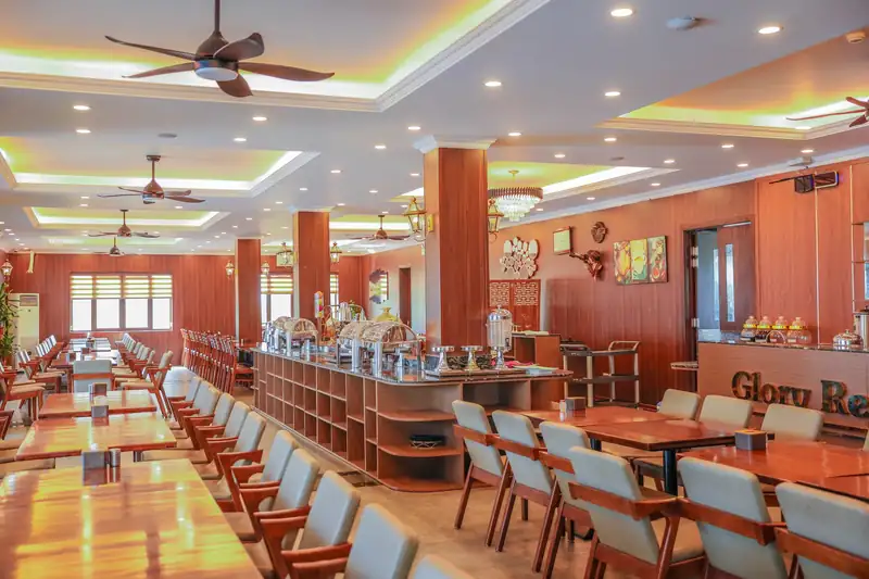 Nhà hàng Glory Resort ốp gỗ với dãy bàn dài, quầy món ăn giữa phòng và trần đèn vàng ấm