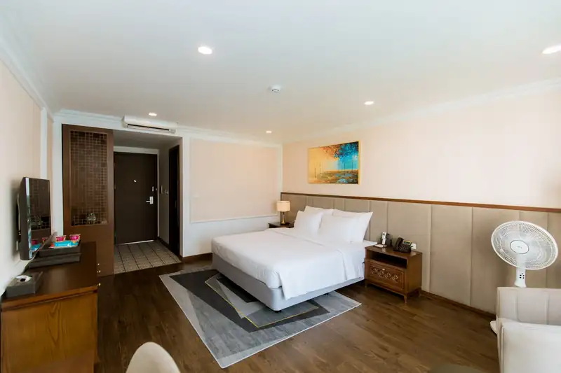 Phòng Deluxe King Pool View nhìn từ cửa sổ về phía giường, tủ gỗ và cửa ra vào