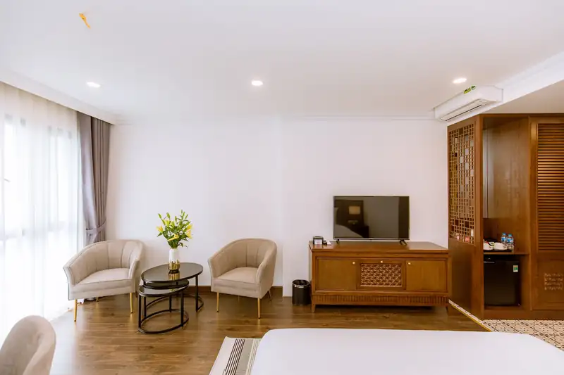 Góc tiếp khách phòng Deluxe King Pool View: hai ghế bành, bàn kính, tủ ti vi và tủ gỗ chạm