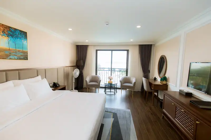Phòng Deluxe King Pool View giường lớn, bàn trà cạnh cửa kính mở ra ban công