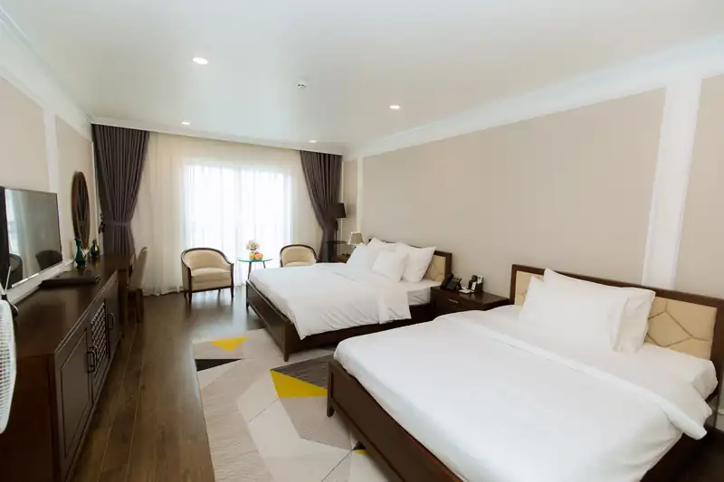 Phòng Deluxe Twin Pool View nhìn chéo: hai giường, ghế bành cạnh cửa kính và tủ gỗ