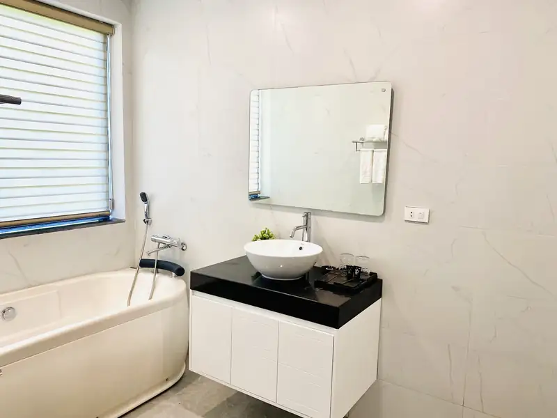 Phòng tắm LakeSide Villa có bồn tắm, lavabo đặt bàn đá đen và gương