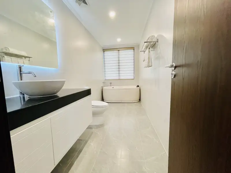 Phòng tắm Osaka Villa: lavabo đặt bàn đá đen, vách kính vòi sen và gương đèn hắt