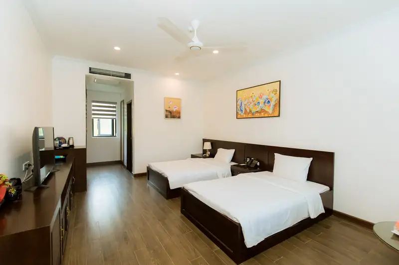 Phòng Standard 2G Garden nhìn từ cửa: tủ ti vi gỗ, hai giường và ô cửa sổ cuối phòng