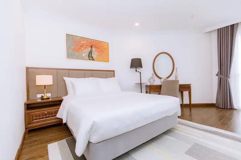 Phòng Standard Pool View giường đôi, đèn bàn, gương tròn và bàn trang điểm gỗ cạnh rèm cửa