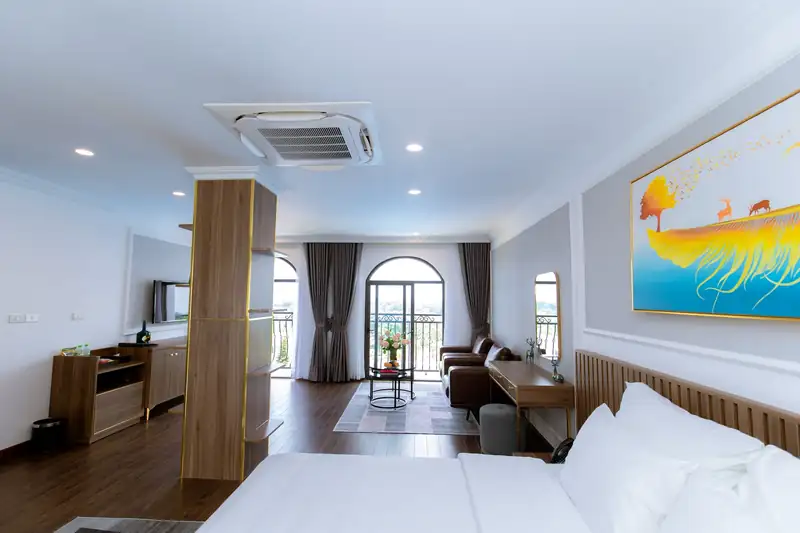 Phòng Suite Pool View nhìn từ giường: cột gỗ, bàn làm việc, sofa và cửa vòm ra ban công