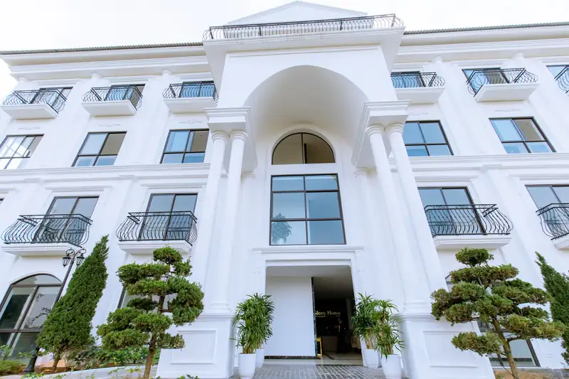 Mặt tiền tòa Home Garden khu Garden View: tòa nhà trắng cửa vòm, ban công sắt uốn, cây tùng cắt tỉa trước sảnh