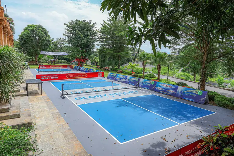 Sân pickleball ngoài trời mặt sân xanh dương tại Glory Resort, bao quanh là cây lớn