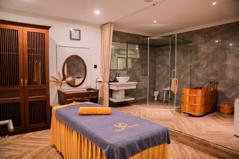 Phòng spa với giường massage, bồn gỗ ngâm chân và phòng tắm vách kính