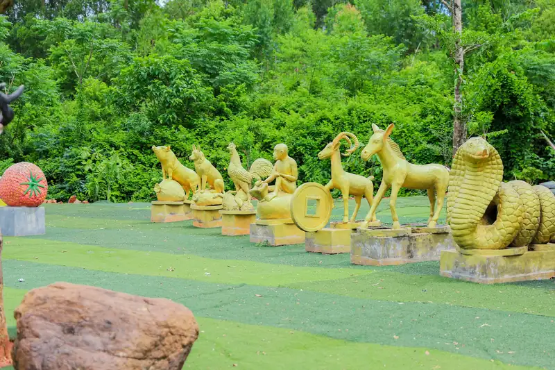 Tượng 12 con giáp màu vàng xếp hàng trên thảm cỏ, phía sau là rừng cây