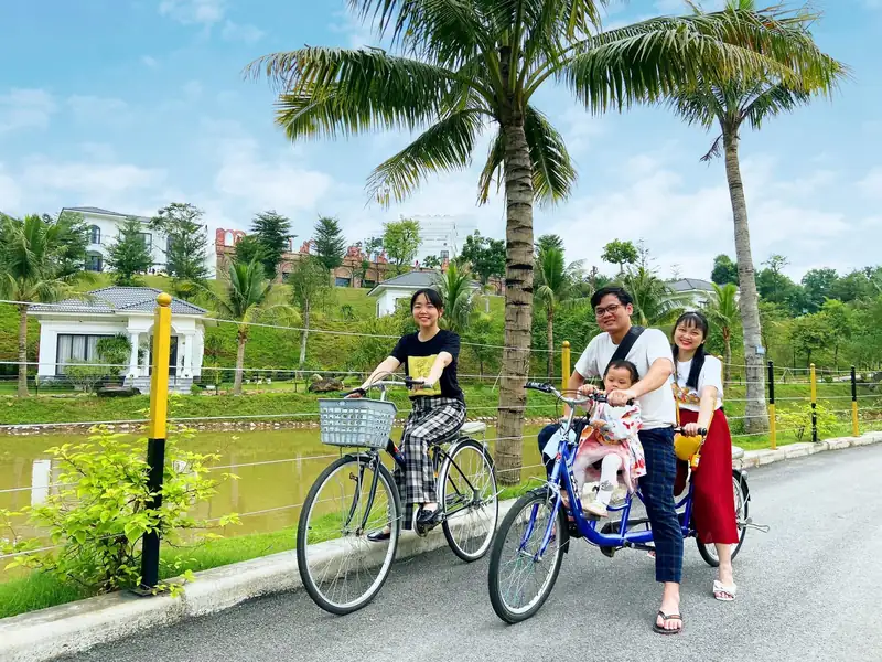Gia đình đạp xe đạp đôi trên đường ven hồ, hàng dừa và biệt thự phía sau